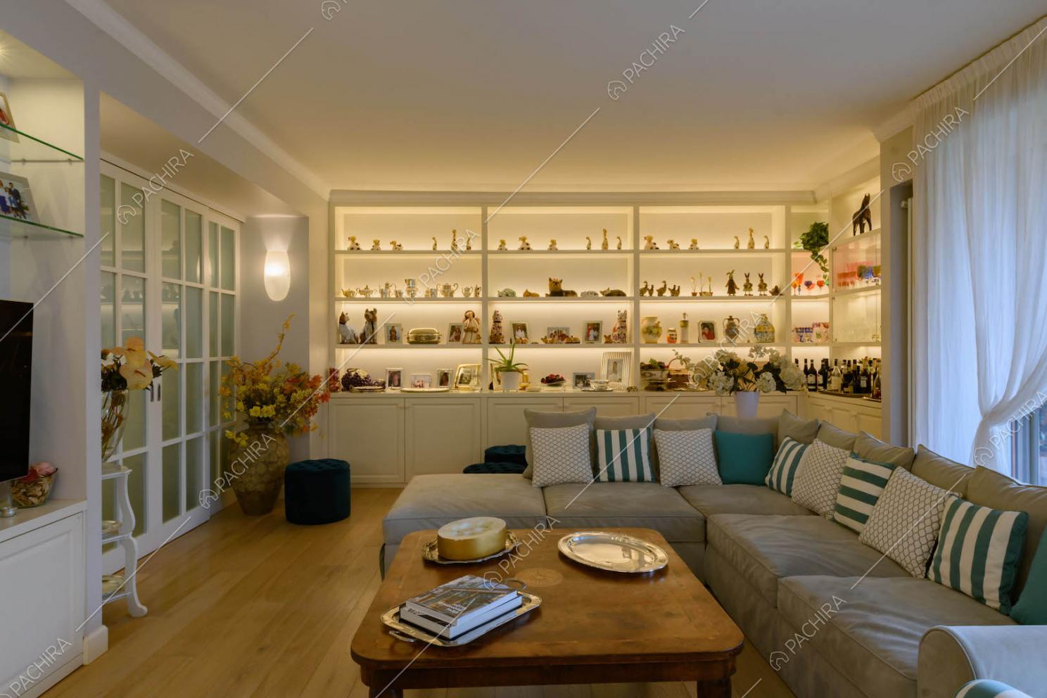 Salotto con divano grigio angolare, pavimento in parquet e porta in vetro con infissi bianchi