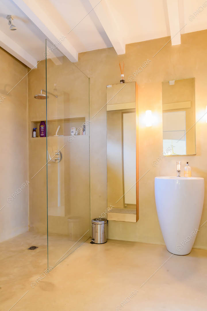 Bagno con box doccia, soffitto con travi a vista e pavimento in cemento lisciato