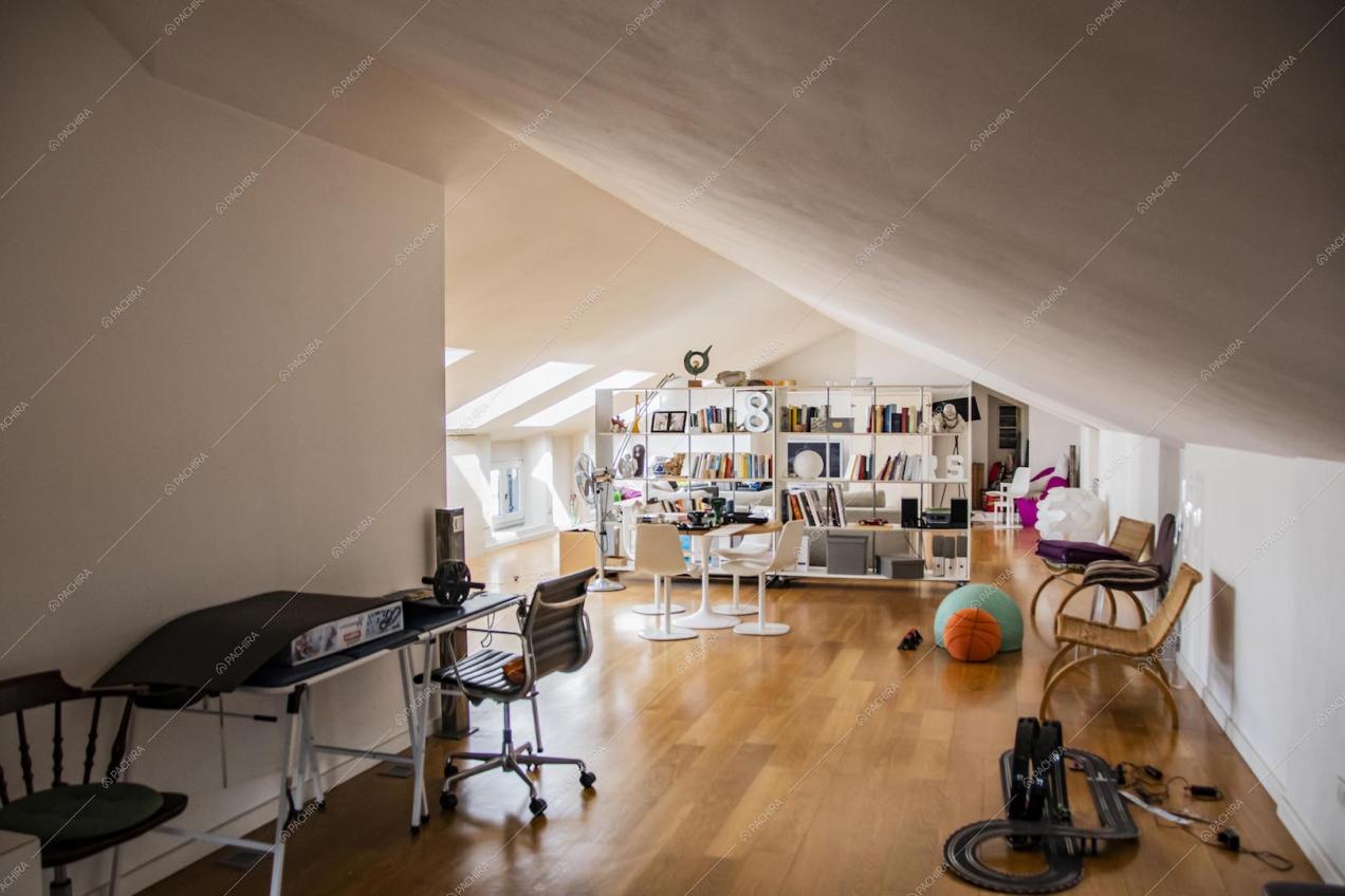 Mansarda dalle pareti e soffitto bianchi, pavimento in parquet e libreria che separa gli ambienti