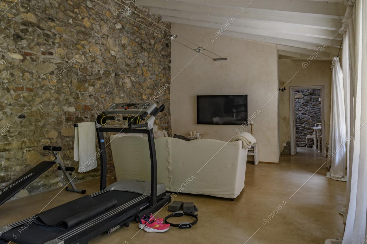Salotto con pavimento in cemento lisciato, parete in pietra e soffitto con travi in legno bianco a vista