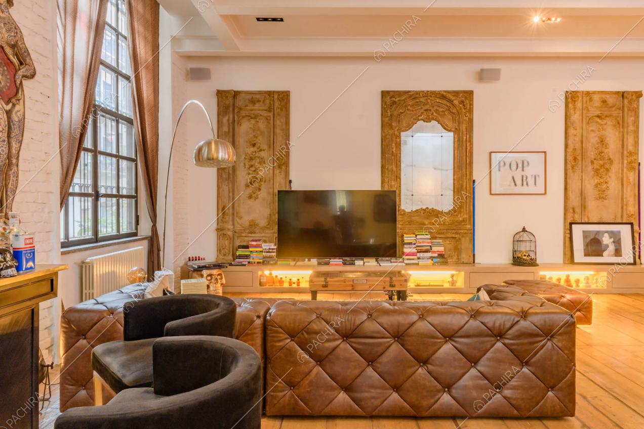 Luminoso salotto con pavimento in parquet, divano marrone in pelle e specchio con cornice dorata