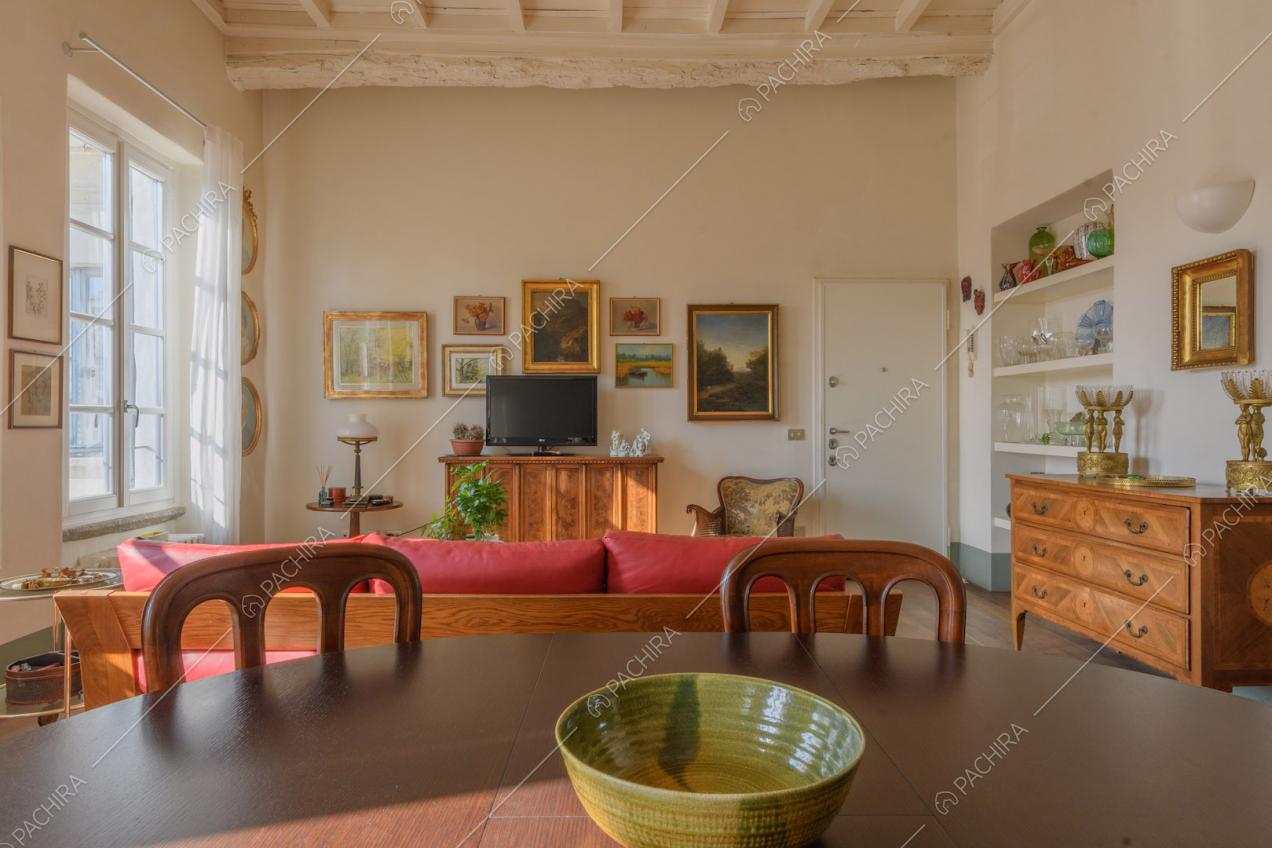Dal tavolo da pranzo in legno vista sul divano rosso e sulle pareti bianche della zona living