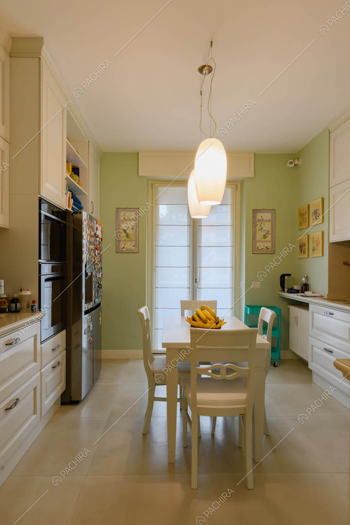 Cucina con parete verde, tavolo da pranzo bianco e porta-finestra