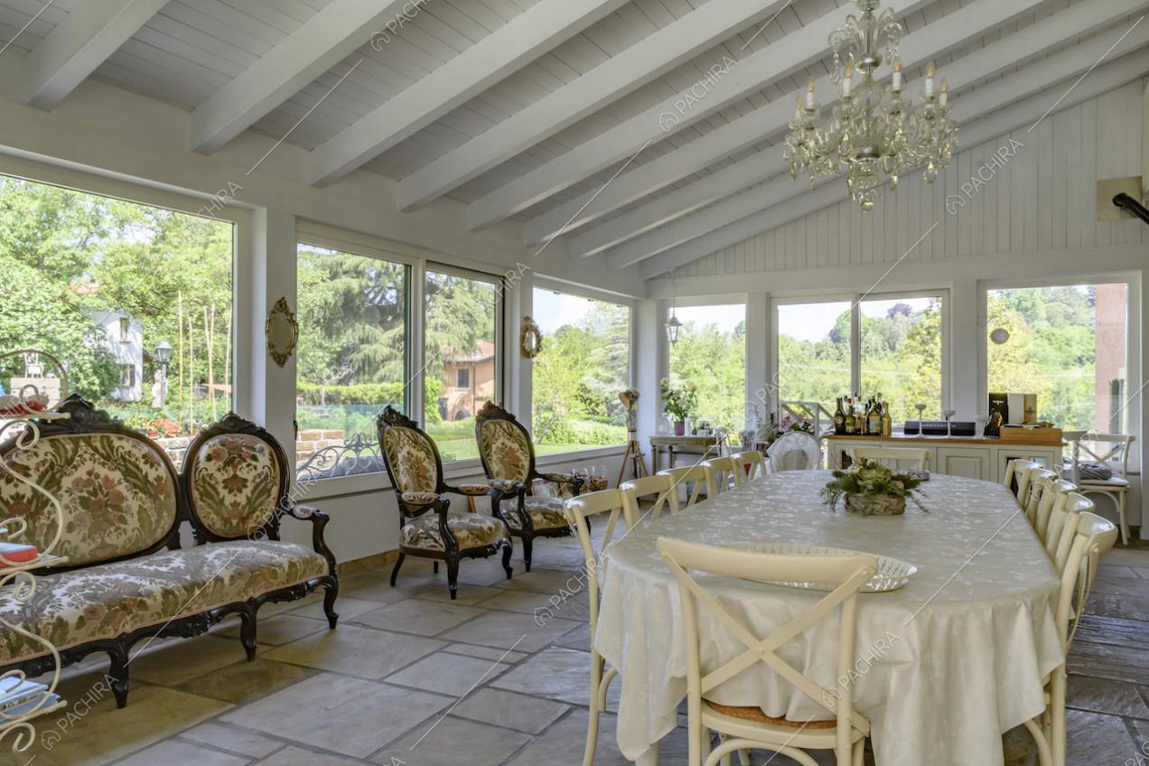 Ampio tavolo da pranzo e divanetti classici, nella veranda illuminata dalle vetrate