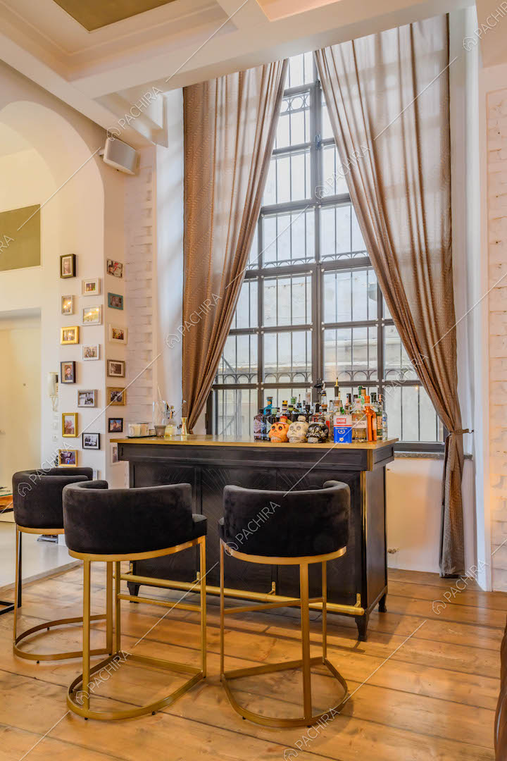 Bancone da bar e sgabelli neri nella sala con pavimento in parquet e finestra in stile industriale
