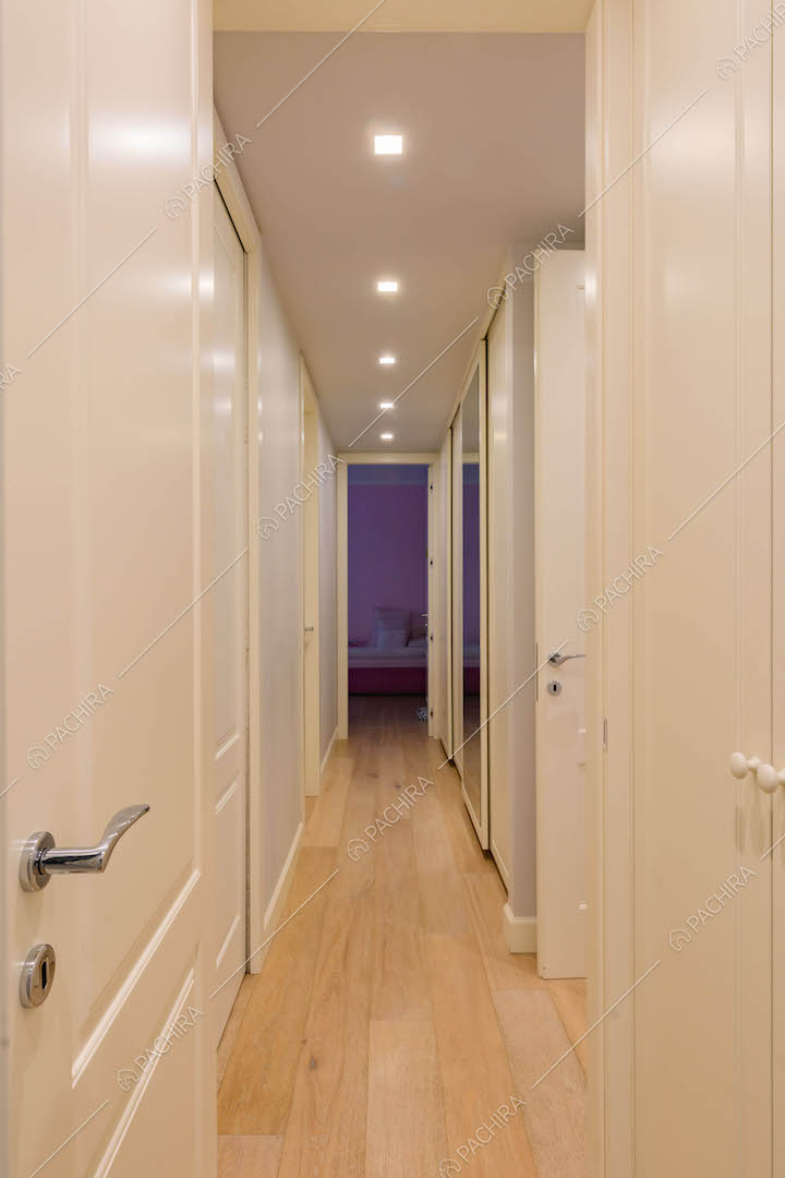 Lungo corridoio con pavimento in parquet e porte bianche con boiserie