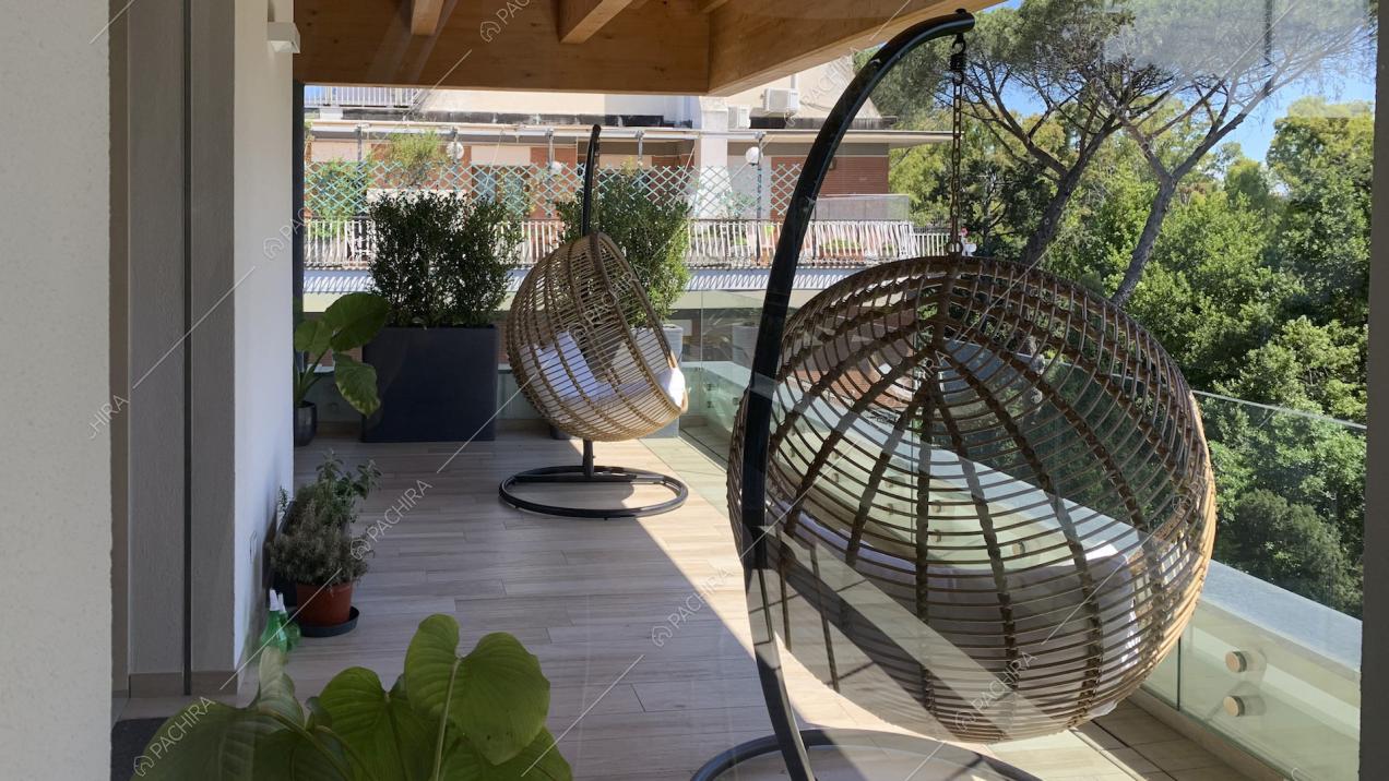 Poltrone di design sospese sul terrazzo con travi a vista, parquet e piante in vaso
