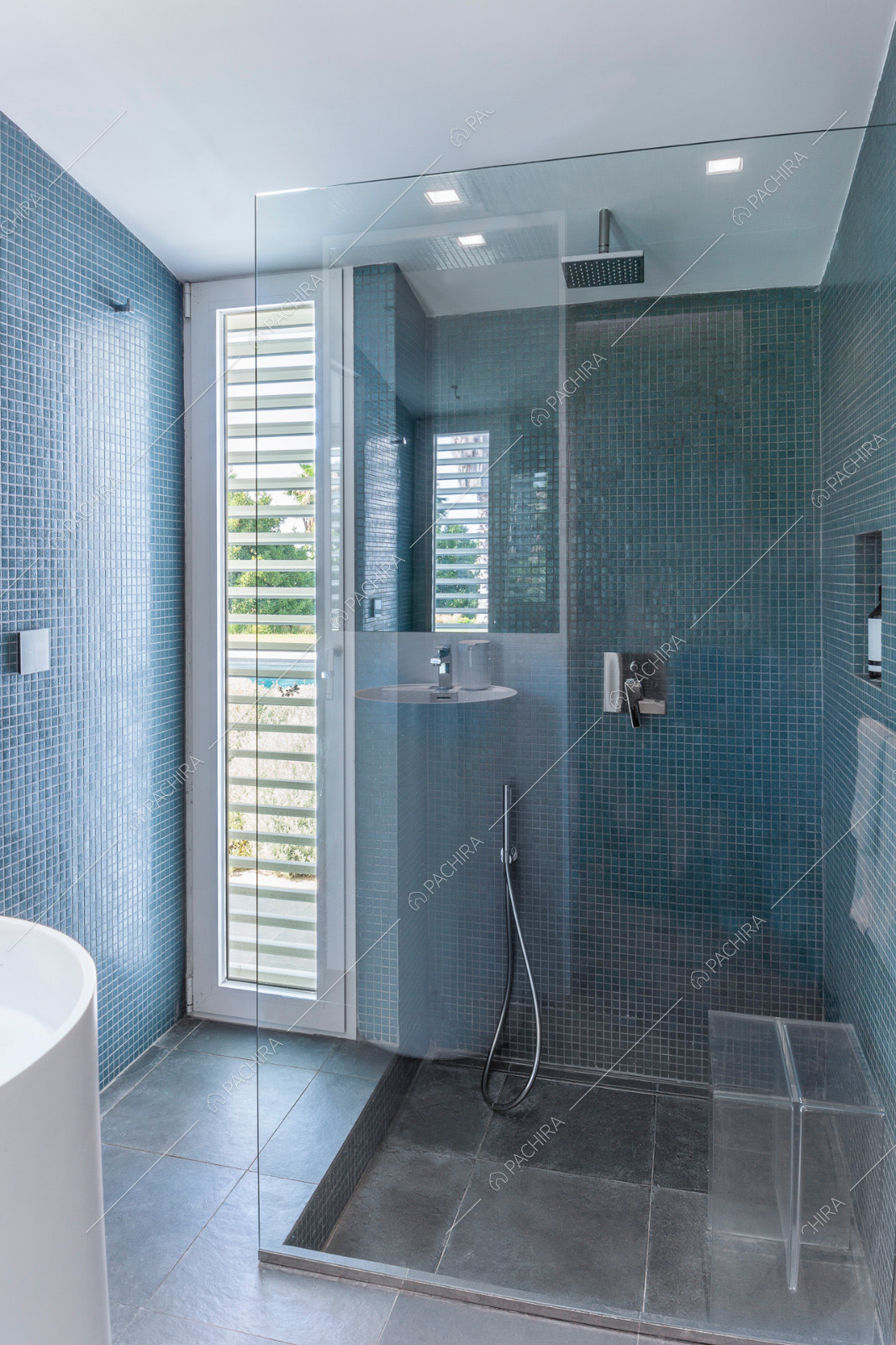 Bagno con piastrelle blu alle pareti e ampio box doccia con parete in vetro