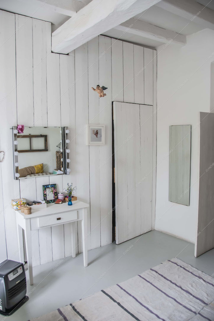 Camera con pareti in legno bianco, comodino e specchio
