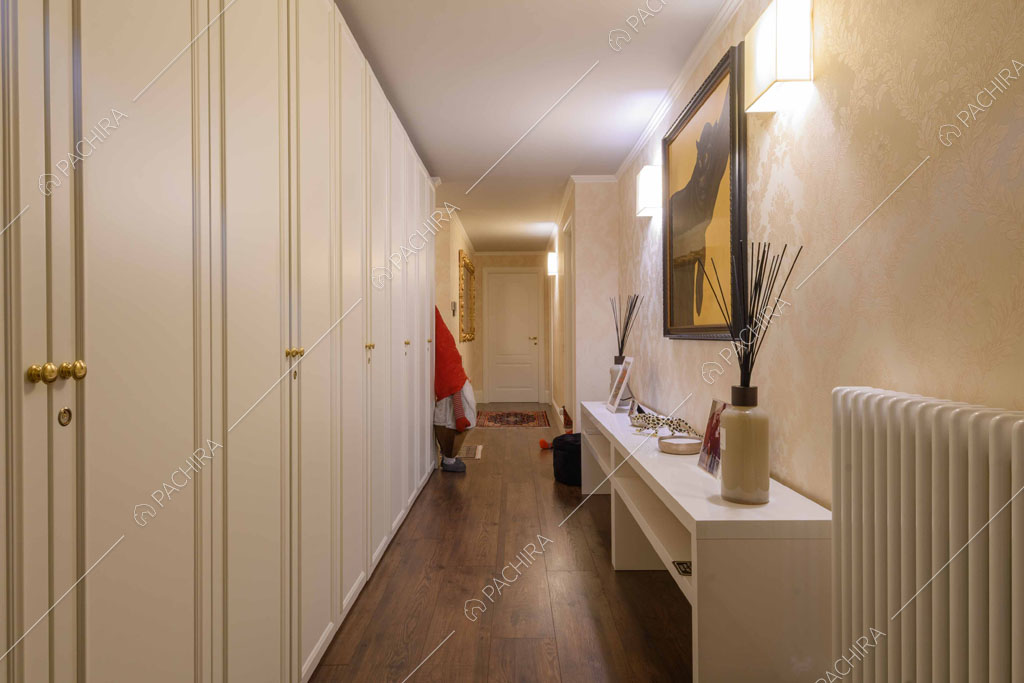 Lungo corridoio con carta da parati, armadi a muro bianchi e pavimento in parquet