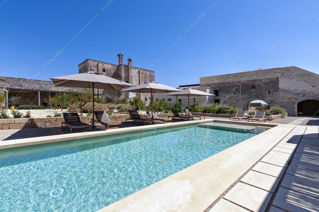Grande piscina rettangolare e area relax nel cortile privato della masseria