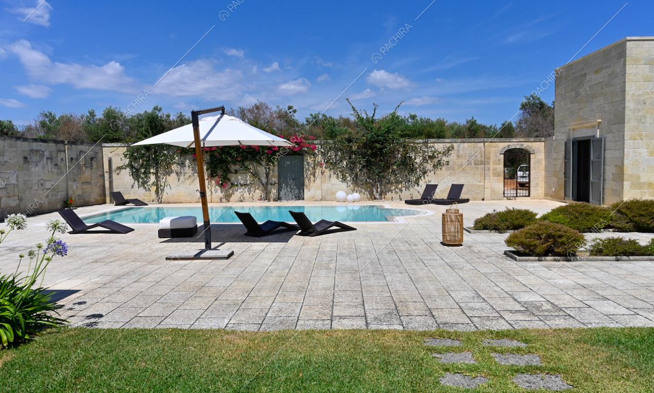 Piscina con ombrellone e lettini nel cortile con pavimentazione in pietra