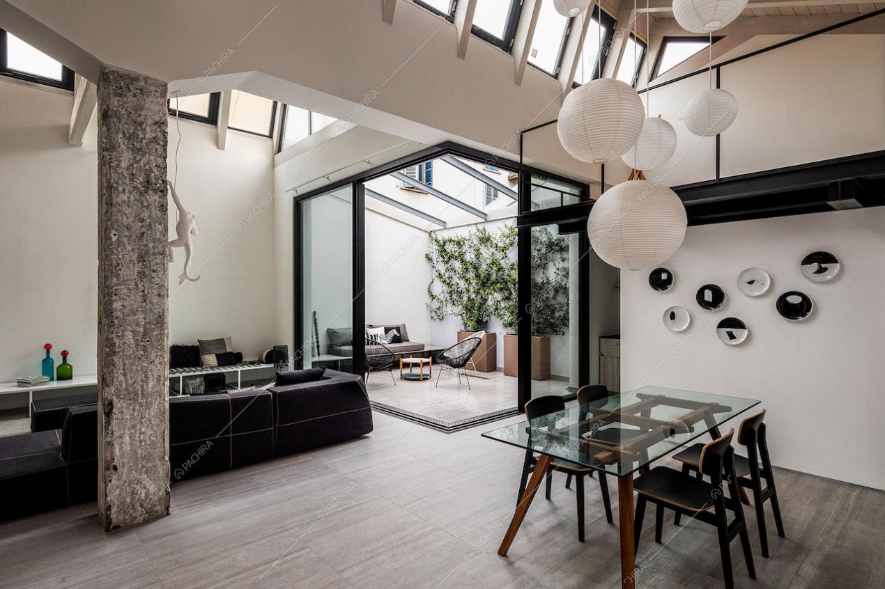 Sala con tavolo da pranzo con piano in vetro, lampadario bianco di design e giardino d'inverno