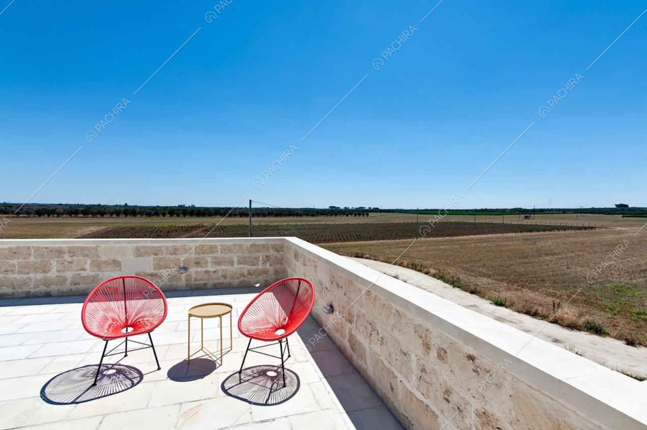 Muretto in pietra, sedie tonde rosse da esterni e vista sulla campagna 