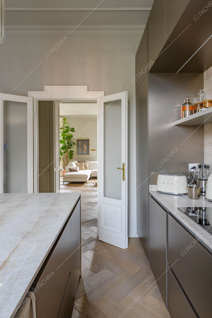 Isola in marmo e fornelli a induzione nella cucina con pavimento in parquet e vista sulla sala