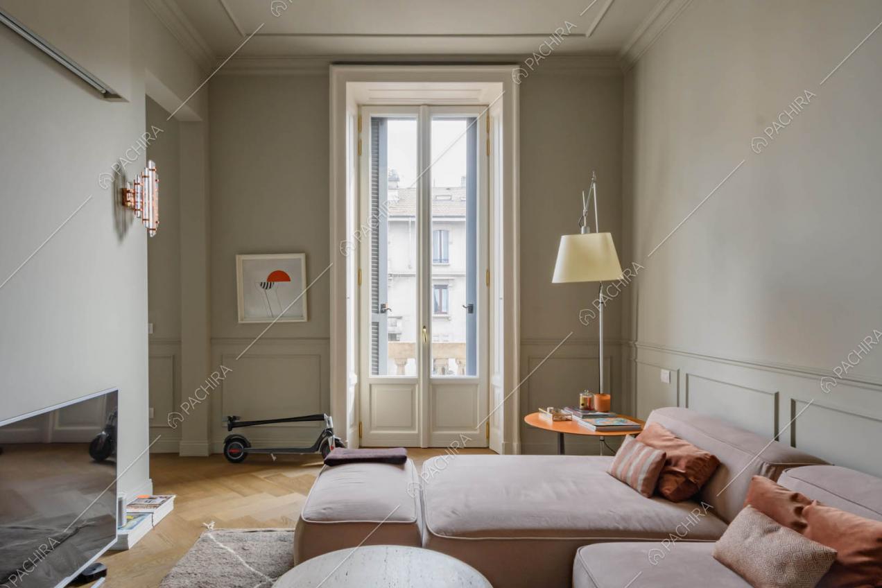 Luminoso salotto con divano angolare rosa, boiserie su pareti e soffitto e porta-finestra