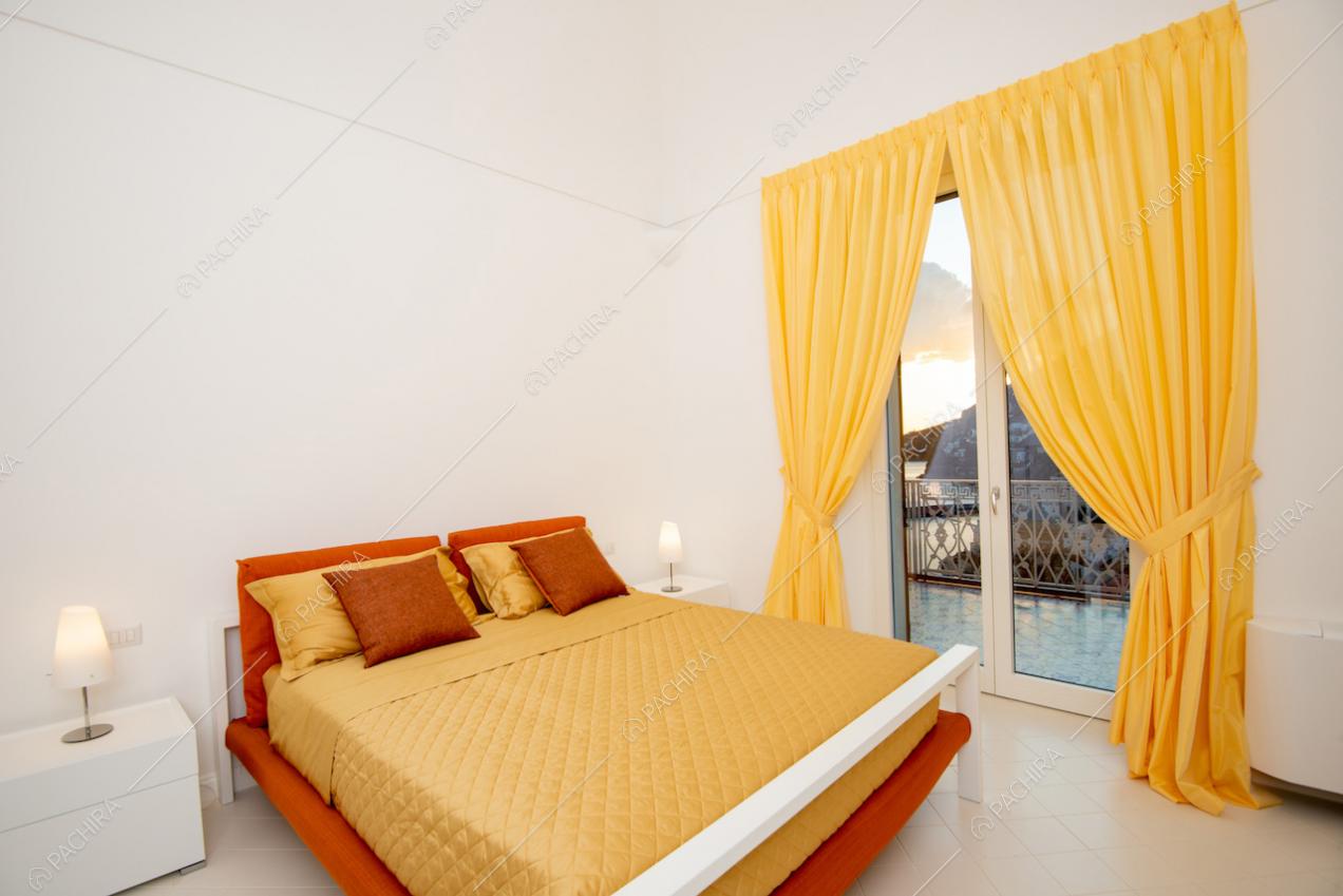 Letto matrimoniale e finestra con tenda gialla e vista sul mare