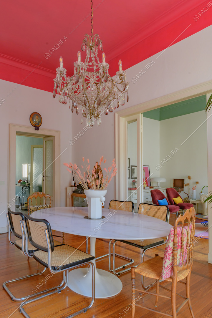 Sala da pranzo con lampadario antico, soffitto fucsia, tavolo bianco e vista sul salotto