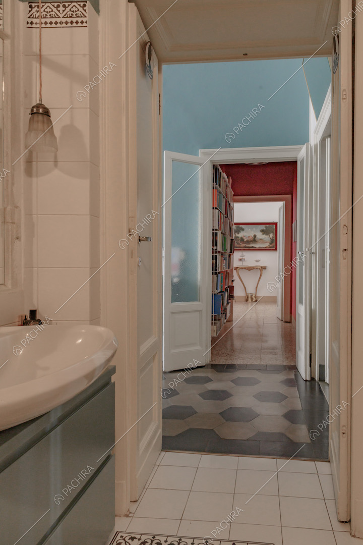Bagno con pavimento in piastrelle bianche, mobile verde e vista sull'atrio con pavimento in marmo