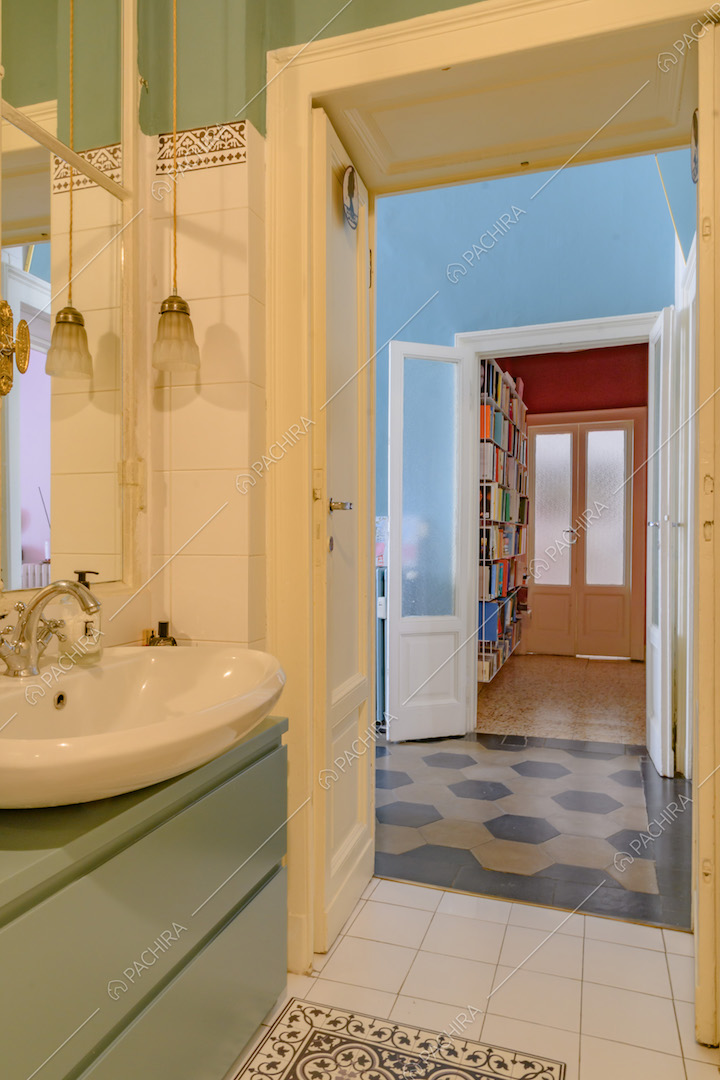 Bagno con piastrelle bianche, mobile verde e vista sull'atrio con pavimento in marmo