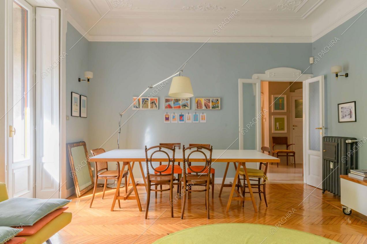 Dal divano del salotto vista sul tavolo da pranzo nella sala dalle pareti azzurre e boiserie sul soffitto