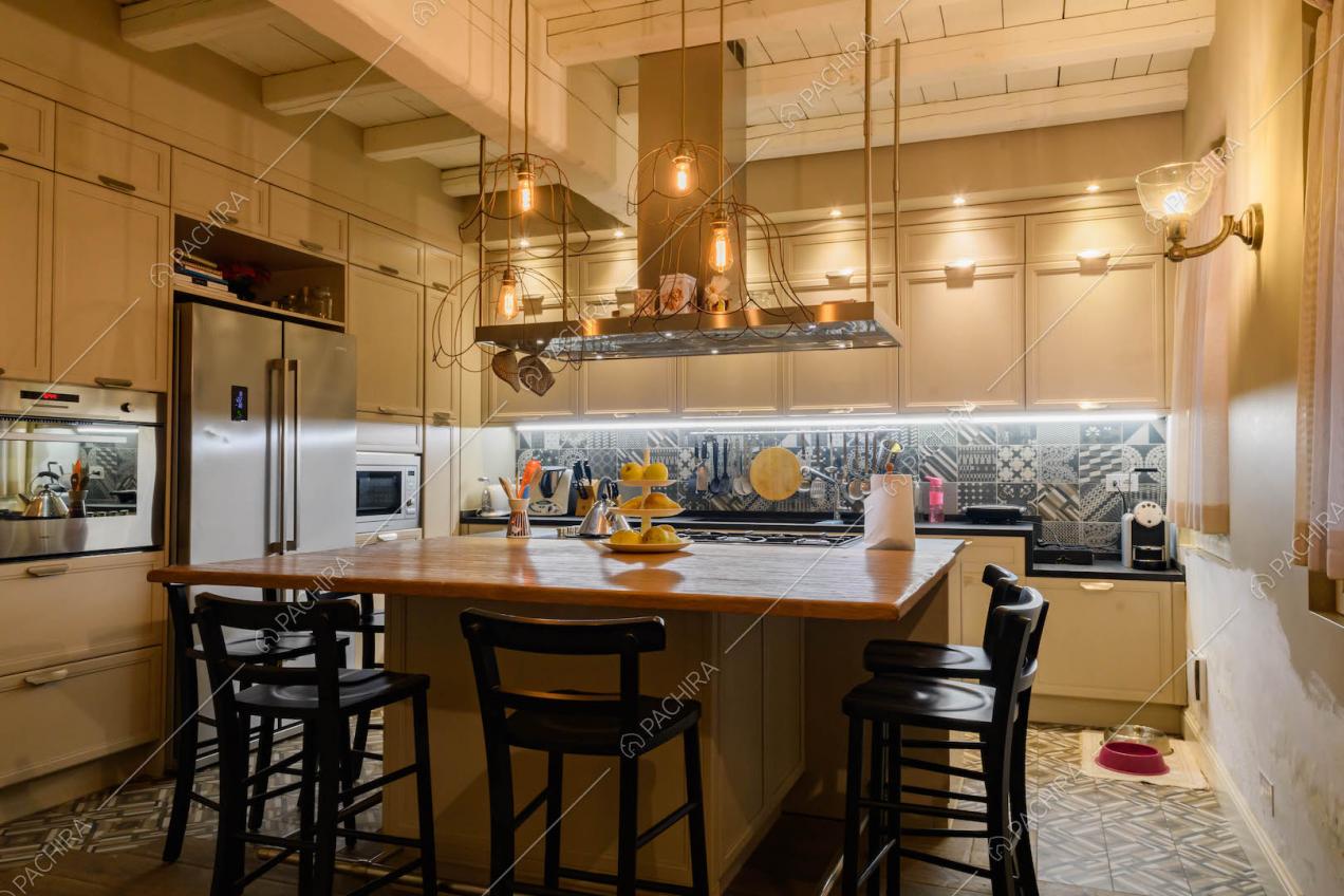 Cucina a isola con bancone in legno, sgabelli neri, cementine e soffitto con travi in legno bianco a vista