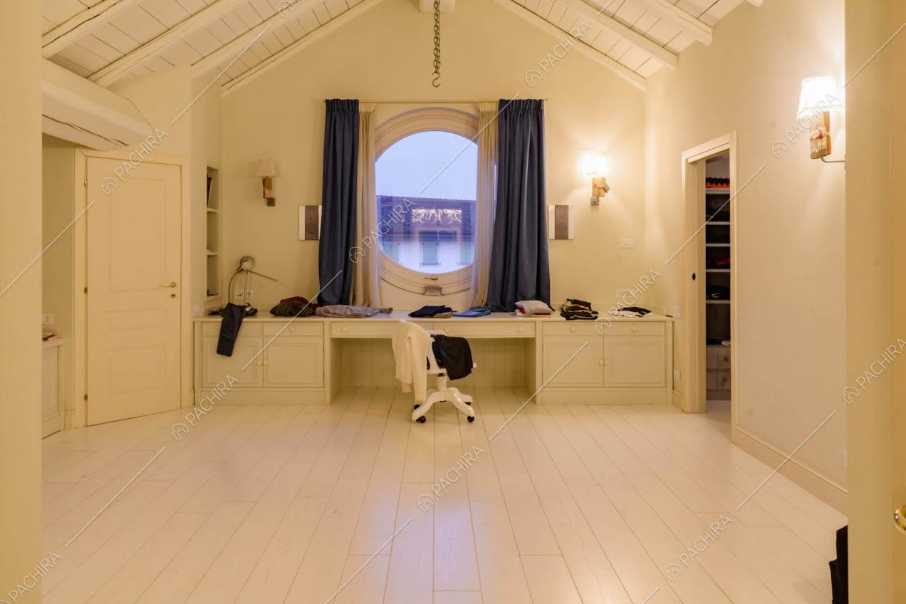 Nella camera da letto parquet bianco, travi in legno a vista e scrivania