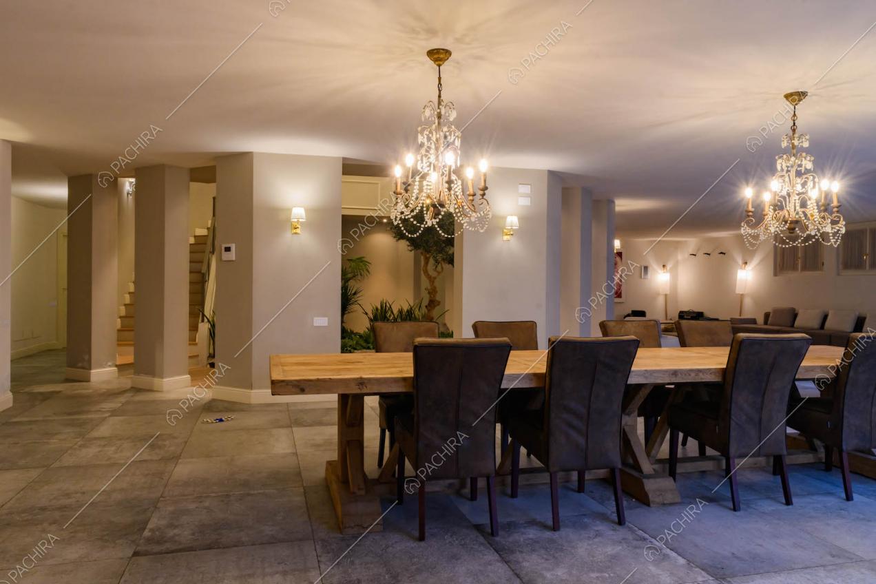 Sala con tavolo da pranzo in legno, cemento in grandi piastrelle grigie e vista sul giardino d'inverno nel vano delle scale