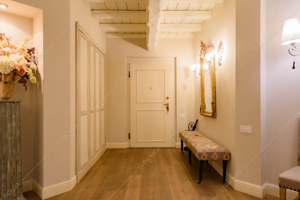 Ingresso della location con porta bianca con boiserie, pavimento in parquet e pareti grigie