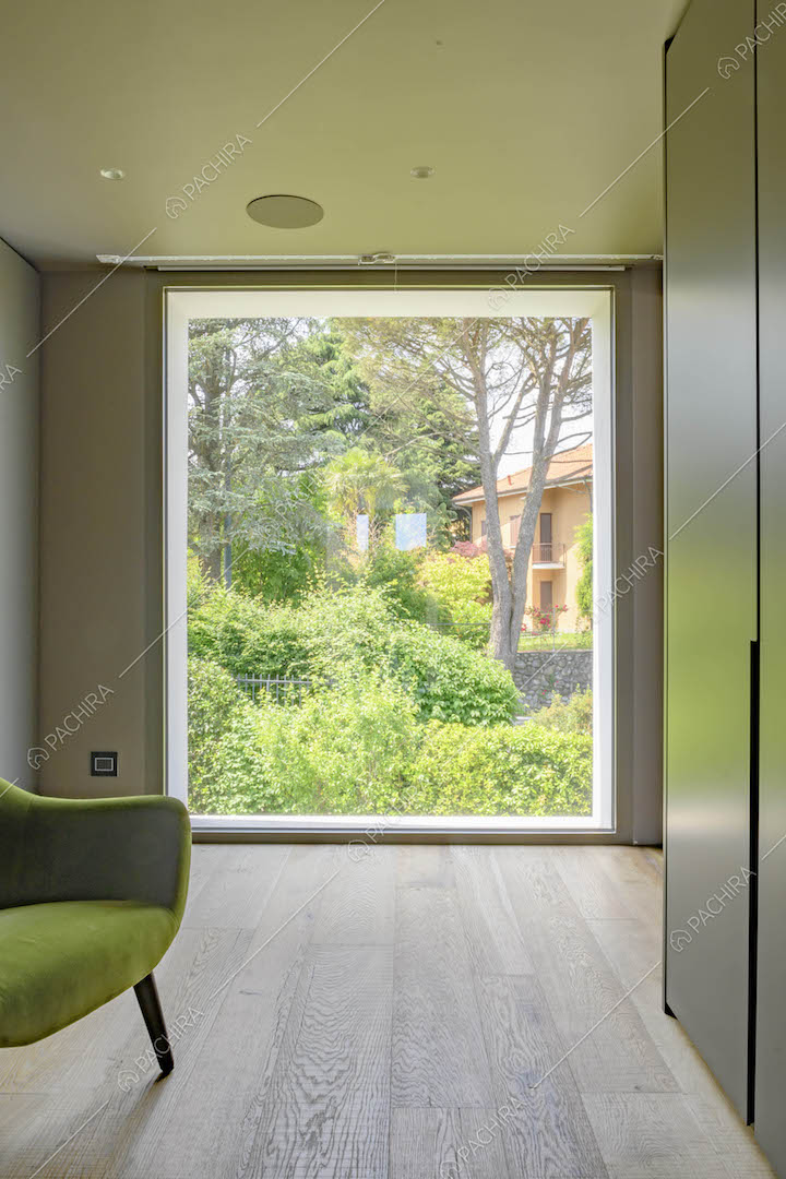 Camera con pavimento in parquet, poltrona verde e grande vetrata con vista sul parco