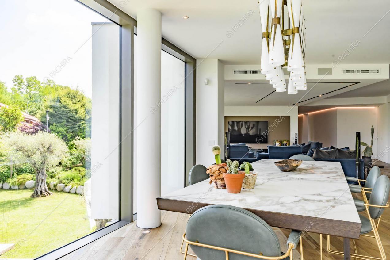 Tavolo da pranzo con piano in marmo nella sala con divani blu, grandi vetrate e pareti bianche