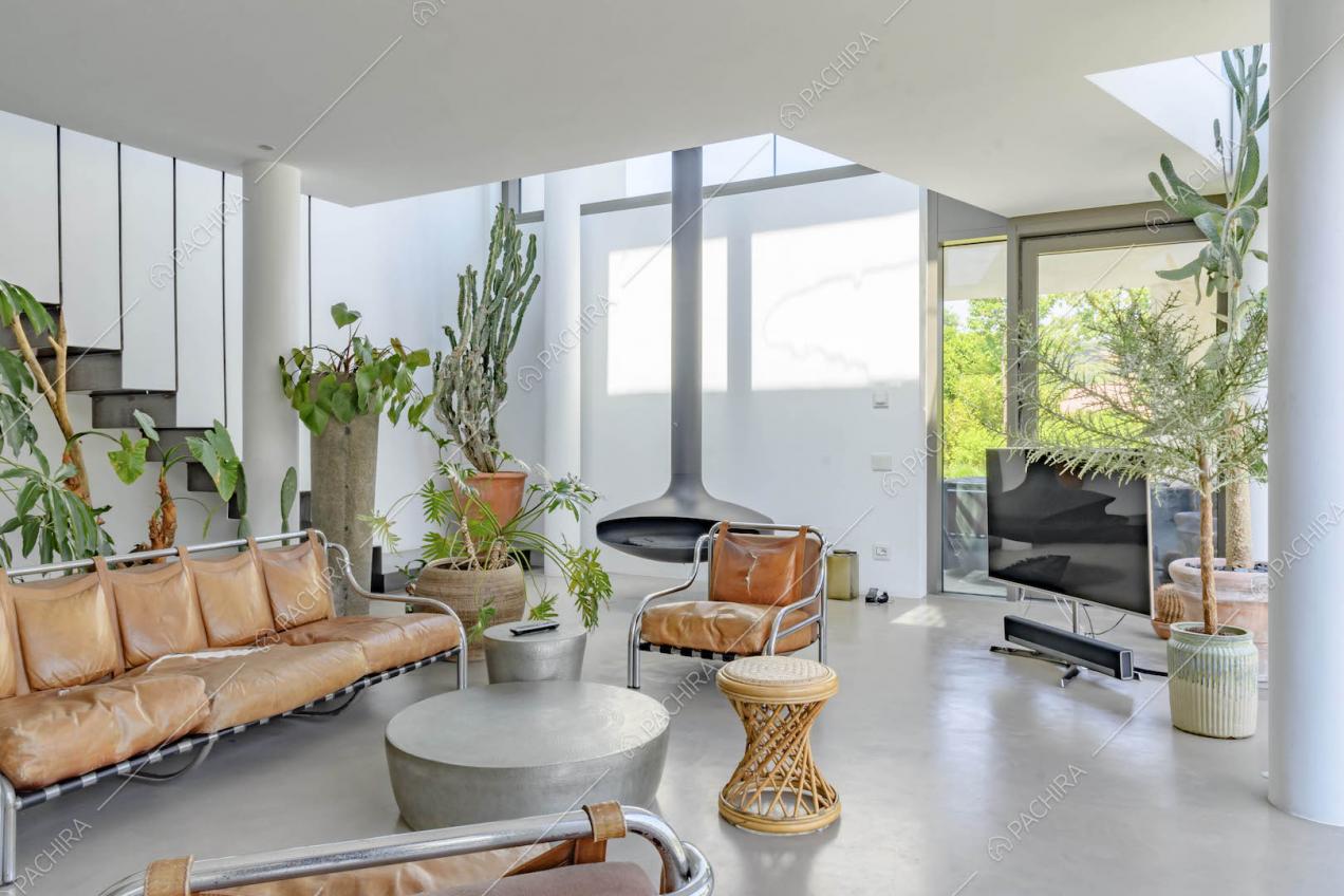 Sala con poltrone e divano di design in pelle marrone, camino sospeso e pavimento in cemento lisciato