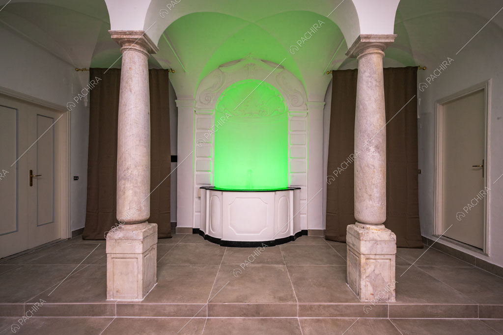 Fontana con boiserie e luce verde neon incorniciata da due colonne