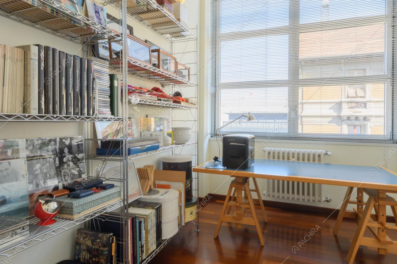 Luminoso studio con libreria in metallo, scrivania, pareti bianche e pavimento in parquet