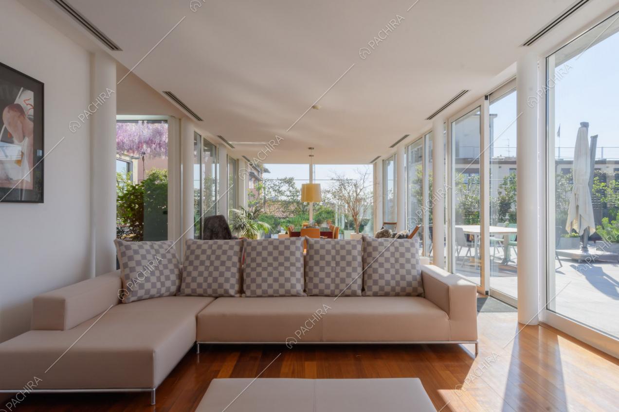 Divano angolare beige nella grande zona living con pareti in vetro e pavimento in parquet