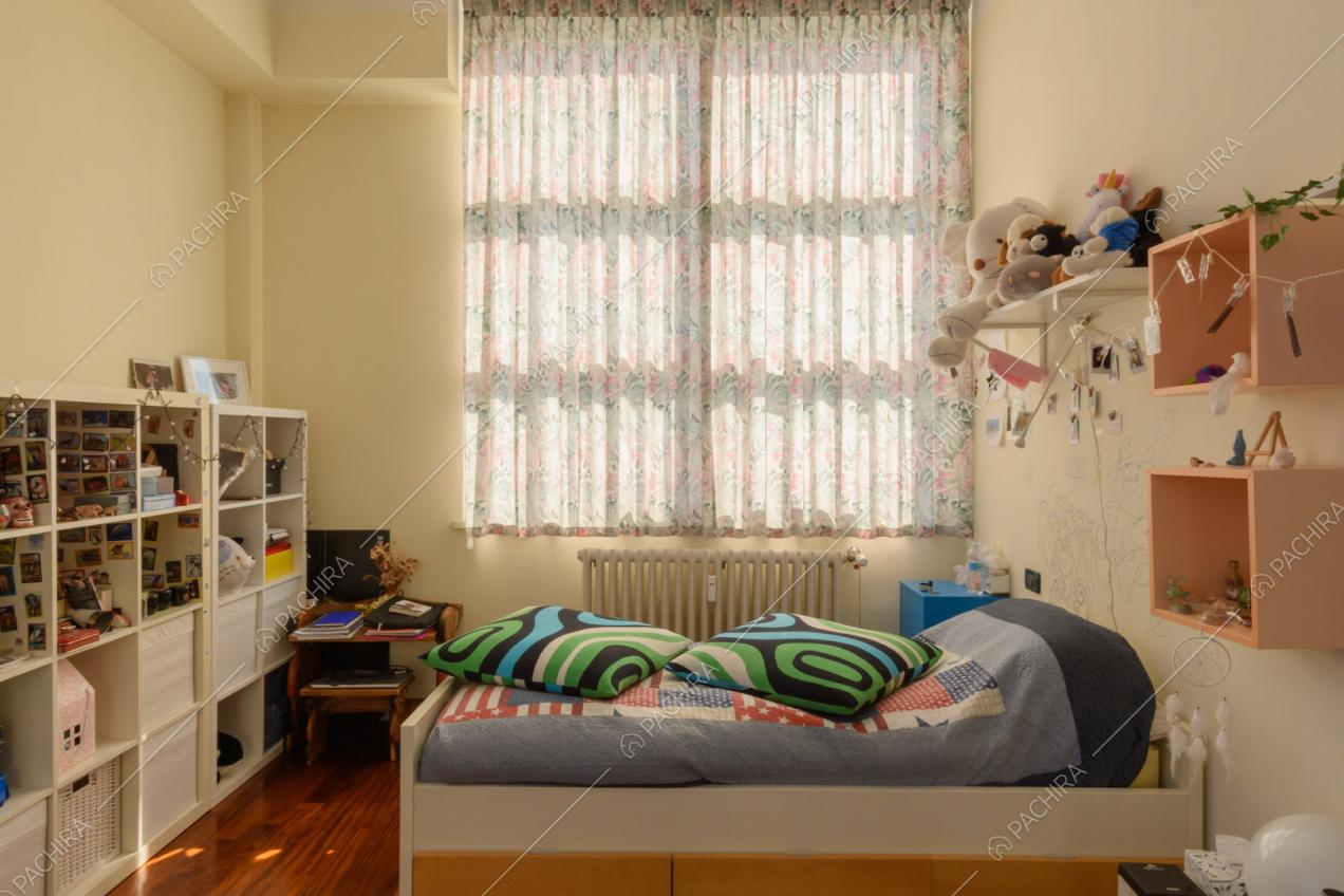 Letto singolo nella luminosa camera con pavimento in parquet, vetrate e libreria