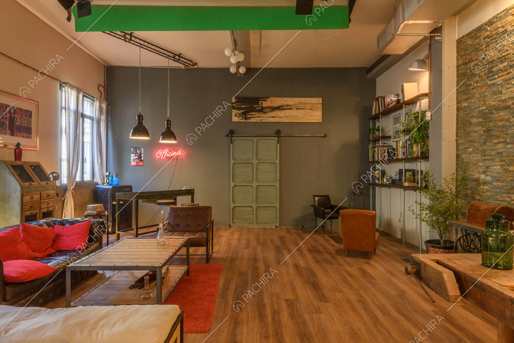 Parete grigia nell'open space con pavimento in parquet, pouf e divano nero in pelle