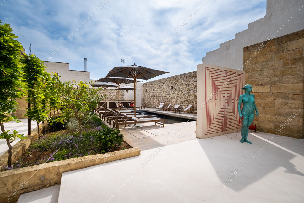 Grande giardino con piante, pietra a vista sul muro, piscina e opera d’arte