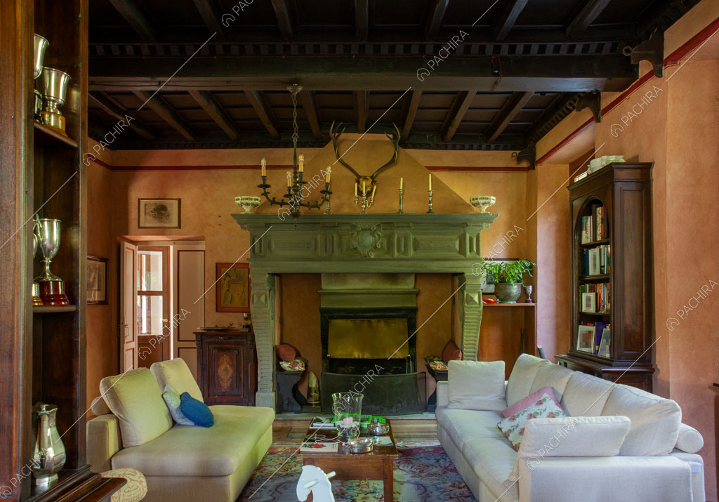 Grande sala con soffitto a cassettoni, divani bianchi e camino con boiserie