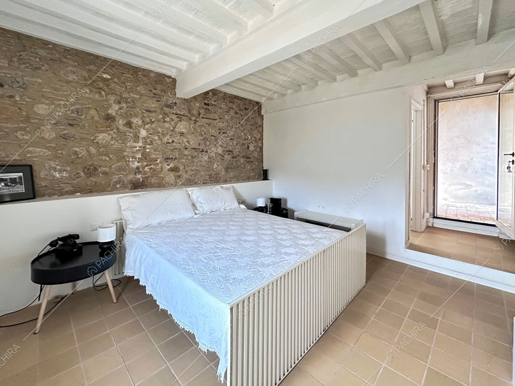 Soffitto in travi bianche in legno a vista e parete in pietra nella camera da letto matrimoniale
