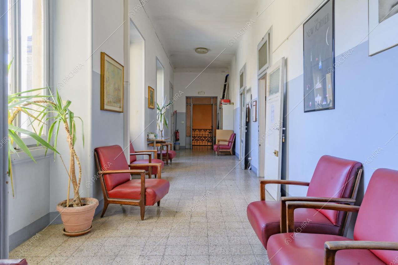 Corridoio con poltrone in pelle rossa, pavimento in piastrelle e pareti azzurre e bianche