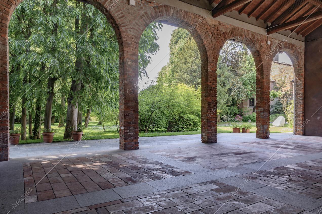 Dal fienile con archi in mattoni rossi, vista sul parco dagli alti alberi e sugli esterni della dimora storica