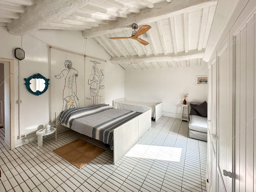 Camera con letto matrimoniale e singolo e travi bianche a vista sul soffitto