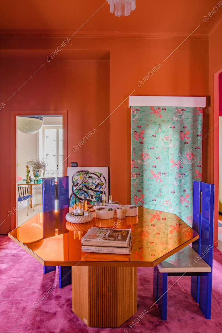 Tavolo arancione e sedie blu elettrico di design nella sala con moquette fucsia