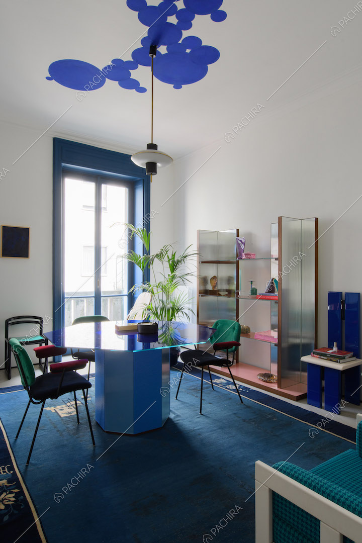 Studio con tavolo azzurro, pareti bianche e porta-finestra blu per accedere al balcone