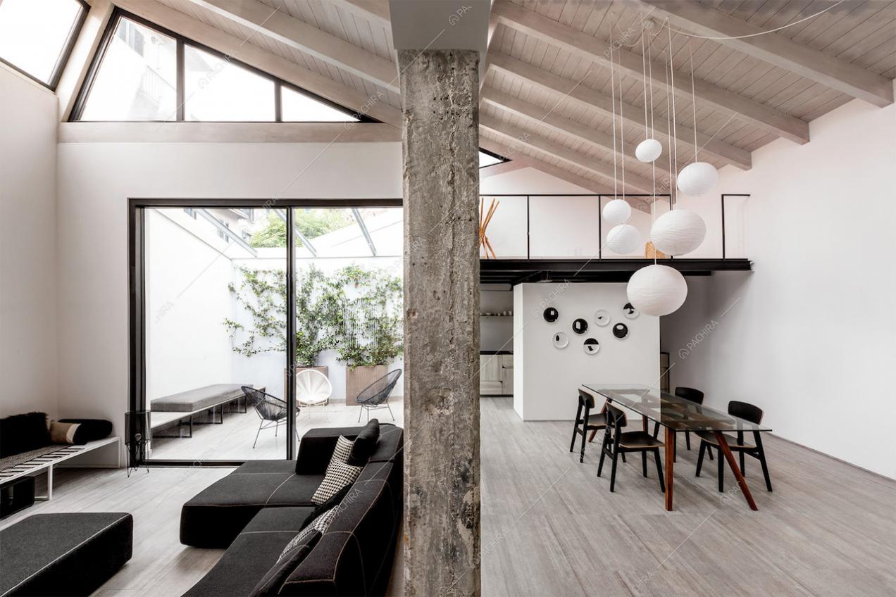 Sala con divano nero, giardino d'inverno, tavolo da pranzo e travi in legno a vista