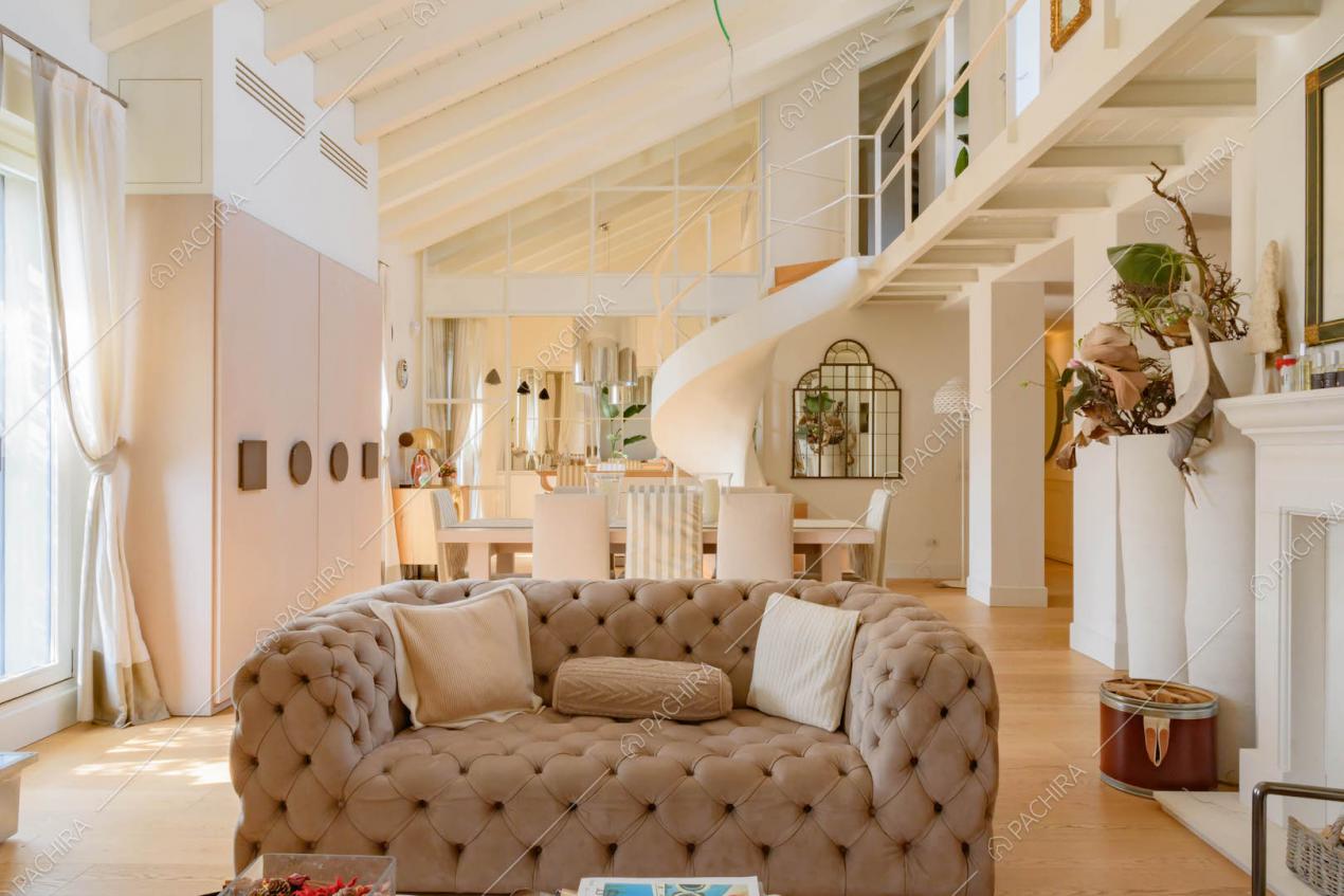 Divanetto marrone nella luminosa zona living con pavimento in parquet e scala a chiocciola