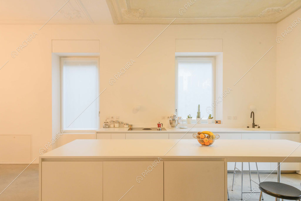Isola bianca con sgabelli nella luminosa cucina total white con boiserie sul soffitto